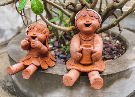 Téléchargez les photos : Une photographie de deux figurines en argile d'une femme et d'un enfant, un pot de fleurs avec des figurines en argile de deux enfants assis sur un pot. - en image libre de droit