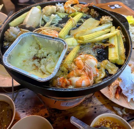 Téléchargez les photos : Une photographie d'un grand pot de nourriture avec une variété de plats, pot chaud de nourriture avec des crevettes, maïs, maïs, et d'autres aliments. - en image libre de droit