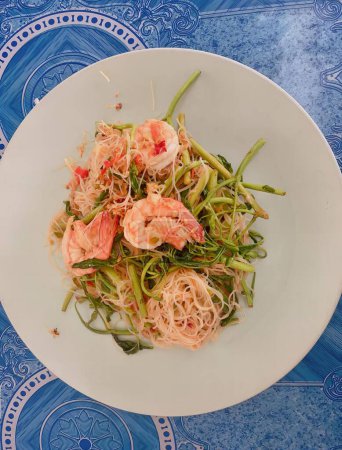 Téléchargez les photos : Une photographie d'une assiette de nourriture avec des nouilles et des crevettes, une assiette de nourriture avec des crevettes et des nouilles sur une nappe bleue. - en image libre de droit