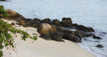 Foto de Una fotografía de una playa con rocas y agua y un barco en la distancia, mar - costa con rocas y arena y un barco en el agua. - Imagen libre de derechos