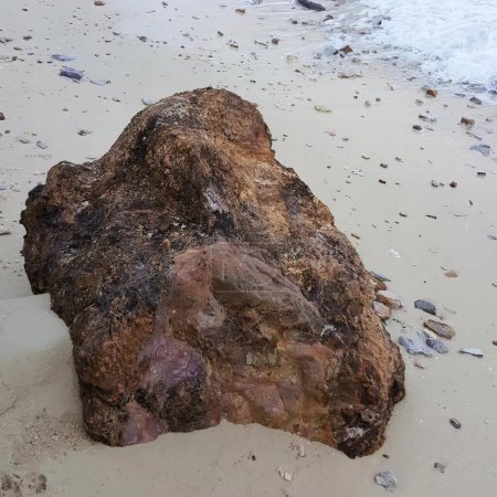 Téléchargez les photos : Une photographie d'un rocher sur une plage avec une vague qui arrive, scène mer-côte avec un grand rocher sur une plage de sable avec des vagues qui s'écrasent. - en image libre de droit