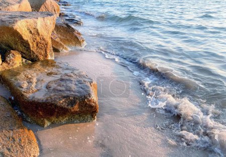 Foto de Una fotografía de una playa con rocas y agua y una ola, orilla del lago con rocas y agua en un día soleado. - Imagen libre de derechos