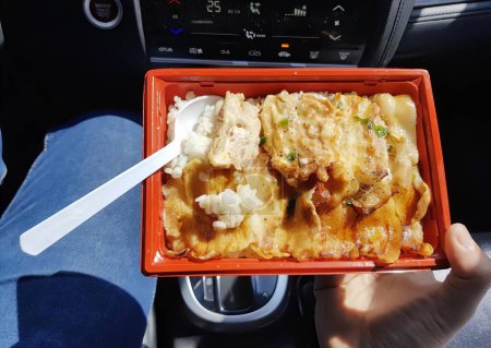 Foto de Una fotografía de una persona sosteniendo una bandeja roja con comida en ella, plato de comida en un coche con una cuchara y tenedor. - Imagen libre de derechos