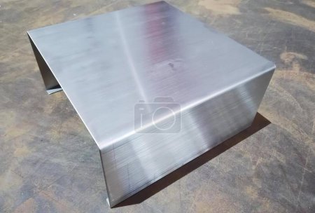 Téléchargez les photos : Une photographie d'une table en métal avec un plateau carré, rôtisseriem d'une boîte en acier inoxydable sur une surface en béton. - en image libre de droit
