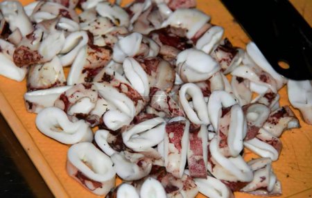 Foto de Una fotografía de una tabla de cortar con calamares en rodajas, nautilusis con cámara en una tabla de cortar con un cuchillo. - Imagen libre de derechos