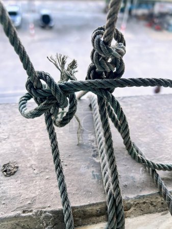 una fotografía de una cuerda atada a un poste con un estacionamiento en el fondo.