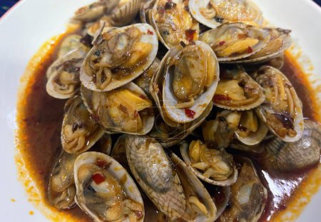 a photography of a plate of clams with sauce and a spoon.