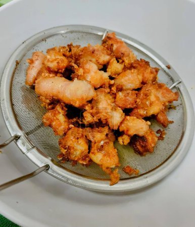 une photographie d'une assiette de crevettes frites dans une passoire.