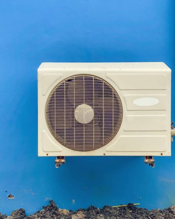 a photography of a white air conditioner sitting on a blue wall.