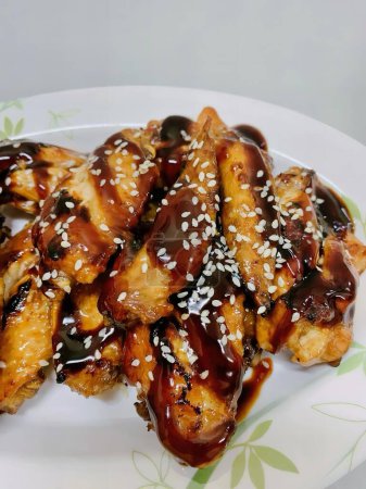 a photography of a plate of chicken wings covered in sauce and sesame seeds.