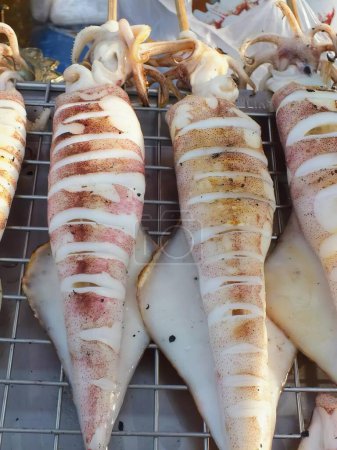 una fotografía de los calamares se cocinan en una parrilla con mucha salsa.