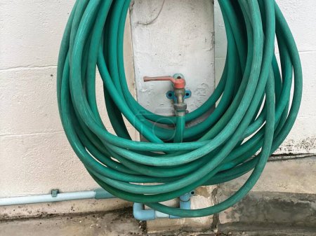 a photography of a green hose attached to a white wall.