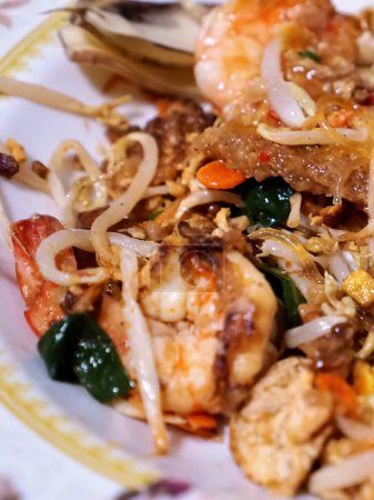 une photographie d'une assiette de nourriture avec des crevettes, des nouilles et des légumes.