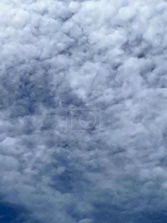 una fotografía de un avión volando a través de un cielo nublado con un cielo azul en el fondo.