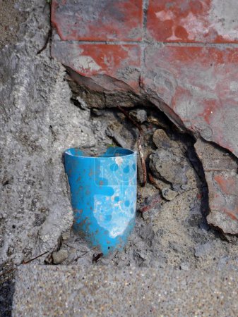 Photo for A photography of a blue cup sitting on the ground next to a brick wall. - Royalty Free Image