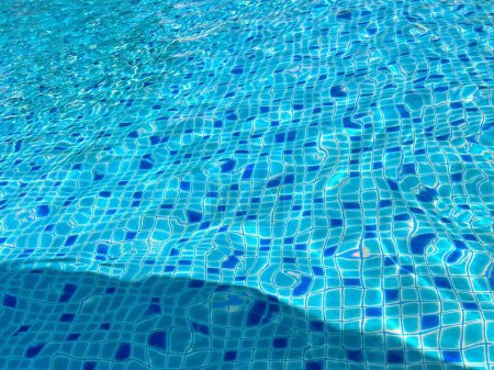 une photographie d'une piscine avec une surface d'eau bleue et l'ombre d'une personne.