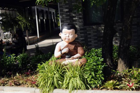 a photography of a statue of a monk sitting in a garden.