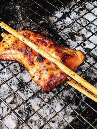a photography of a chicken on a grill with chopsticks.