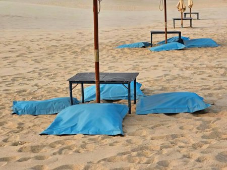 a photography of a beach with blue covers and umbrellas on the sand.