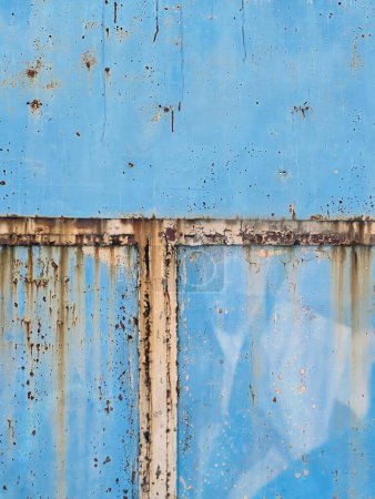 une photographie d'un mur bleu avec rouille et une fenêtre.