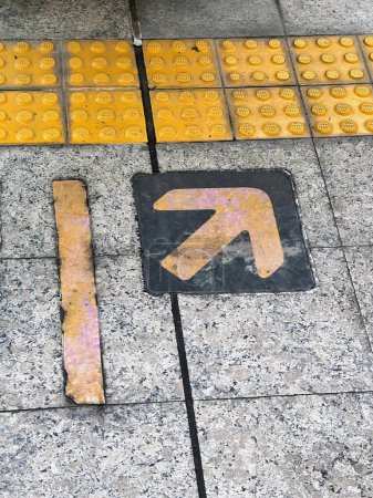 une photographie d'un panneau jaune et noir sur un trottoir.