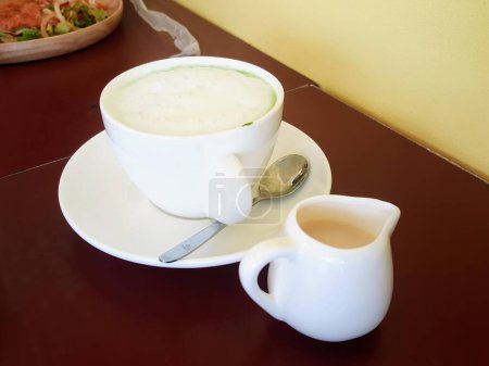 eine Fotografie einer Tasse Kaffee und eines Löffels auf einem Tisch.