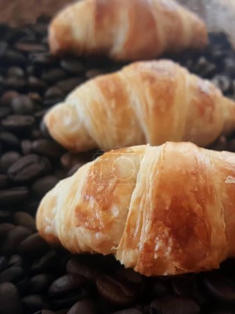 a photography of two croissants on a table with coffee beans.