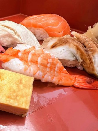 una fotografía de una bandeja roja con una variedad de sushi y camarones.