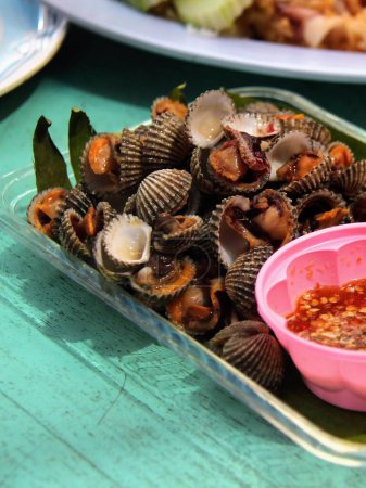 a photography of a plate of clams with a bowl of sauce.