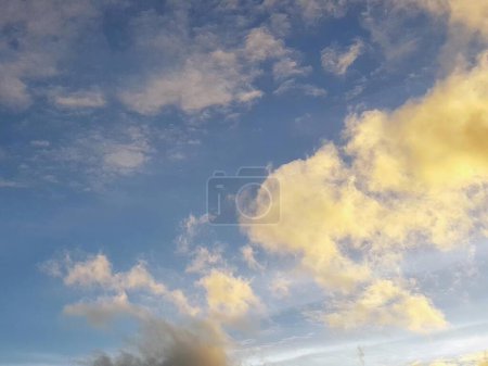 una fotografía de un avión volando a través de un cielo nublado con un cielo amarillo y azul.