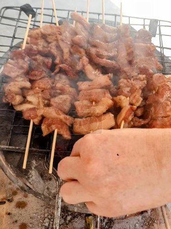 eine Fotografie einer Person, die Fleisch auf einem Grill mit Spießen kocht.