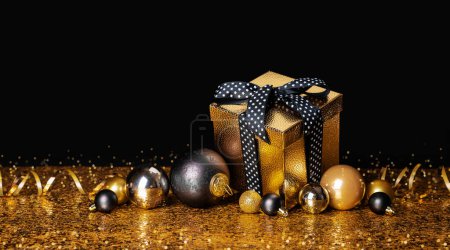 Foto de Felicidades Feliz Navidad y Feliz Año Nuevo. Caja dorada con un regalo y bolas de Navidad sobre fondo negro y dorado - Imagen libre de derechos