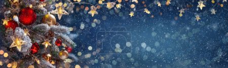 Choinka z bombkami w niebieską noc - dekoracje na gałązkach jodły z błyszczącymi i nieostrymi światłami i płatkami śniegu na abstrakcyjnym tle