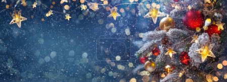 Foto de Árbol de Navidad con adornos en una noche azul - decoraciones en ramas de abeto con luces brillantes y desenfocadas y copos de nieve sobre un fondo abstracto - Imagen libre de derechos