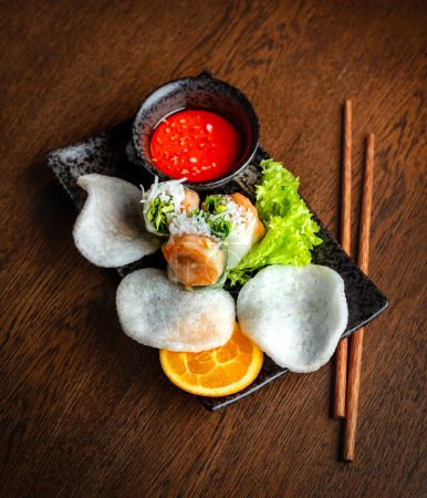 Photo for Asian cuisine. Shrimp and rice rolls, rice bread and hot sauce in black ceramic dishes - Royalty Free Image
