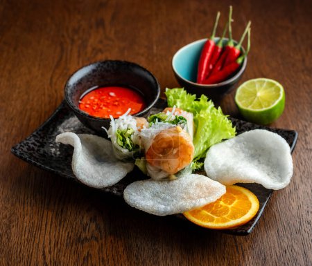 Photo for Asian cuisine. Shrimp and rice rolls, rice bread and hot sauce in black ceramic dishes - Royalty Free Image
