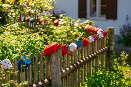 Bunte Metallbecher hängen an einem alten Holzzaun in einem bayerischen Dorf