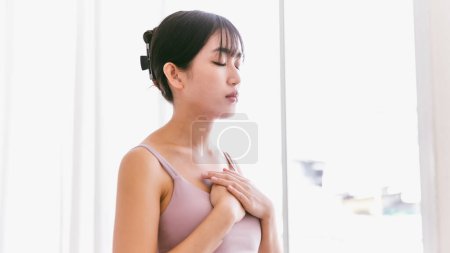 Foto de Retrato de una mujer asiática deportiva con las manos en el pecho y cerrar los ojos, respirar y exhalar, reunirse con el aliento. practicar yoga meditando para la relajación y la atención plena. - Imagen libre de derechos