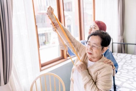 Enfermera cuidadora que usa ejercicios de exfoliación con una mujer asiática mayor mediante el uso de ejercicios de banda de resistencia para la paciente mayor en el tratamiento de fisioterapia. Atención domiciliaria y concepto de hogar de ancianos.