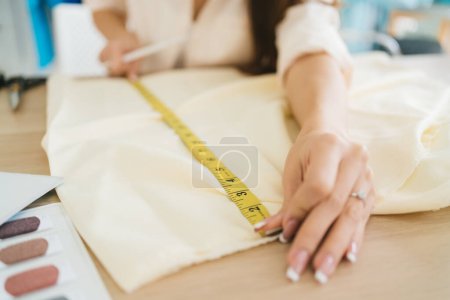 Hands of female fashion designer or tailor hand measuring paper with measuring tape for making clothes pattern. Fashion designer tailor in the workshop working for a new collection.