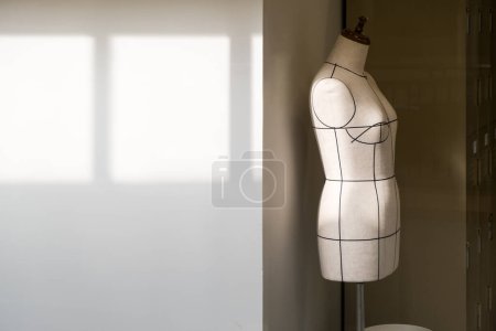 Foto de Empty tailor's textile female mannequin with black lines with sunlight on it for dressmaker working and designing new fashion collections with patterns and draping in an atelier tailor workshop. - Imagen libre de derechos
