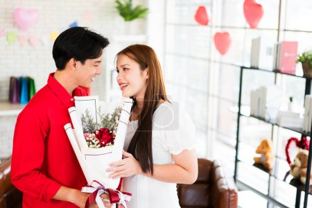 Un joven asiático sorprendió a su novia dándole una rosa y un ramo de flores para su fecha de aniversario en casa. Mujer asiática disfrutar de recibir ramo de su novio. Celebración de San Valentín