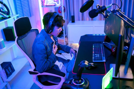 Junge asiatische Mann professionelle Gamer in einer Jeansjacke sitzt auf einem Stuhl und ergreift seine Brust Herzinfarkt leidet unter Stress bei einem Spiel oder Wettbewerb. Konzept des Schmerzes durch Gaming und esports.