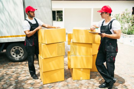 Trabajadores asiáticos y caucásicos en uniforme descargando cajas de cartón del camión. Entrega de hombres descargando cajas y comprobar la lista de verificación con sus compañeros de trabajo. Servicio profesional de entrega y mudanza.