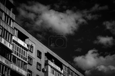 Los últimos pisos de un edificio de ladrillo de varios pisos sobre el fondo de un cielo azul con nubes blancas. Bocetos de la ciudad, jungla de piedra. Foto en blanco y negro