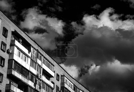 Die letzten Stockwerke eines mehrstöckigen Backsteingebäudes vor dem Hintergrund eines blauen Himmels mit weißen Wolken. Stadtskizzen, Steindschungel. Schwarz-Weiß-Foto