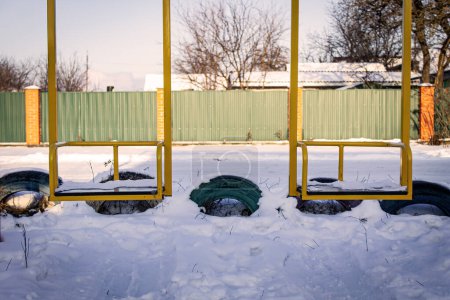Photo for Yellow metal swing on the playground in winter - Royalty Free Image