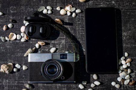Eine Komposition im Stil von Flatlay. Auf schwarzem Hintergrund eine Reihe von Touristen: Kamera, Handy, Kopfhörer. Gegenstände und Muscheln