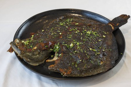 Köstlicher frischer Bio-gebratener Brillenfisch mit Petersilie auf schwarzem Teller
