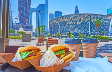 Téléchargez les photos : DUBAI, Émirats arabes unis - 6 MARS 2022 : Savourez de délicieux hamburgers et du café chaud dans un café extérieur avec vue sur Coca-Cola Arena, Burj Khalifa et Address Sky View en arrière-plan, le 6 mars à Dubaï - en image libre de droit